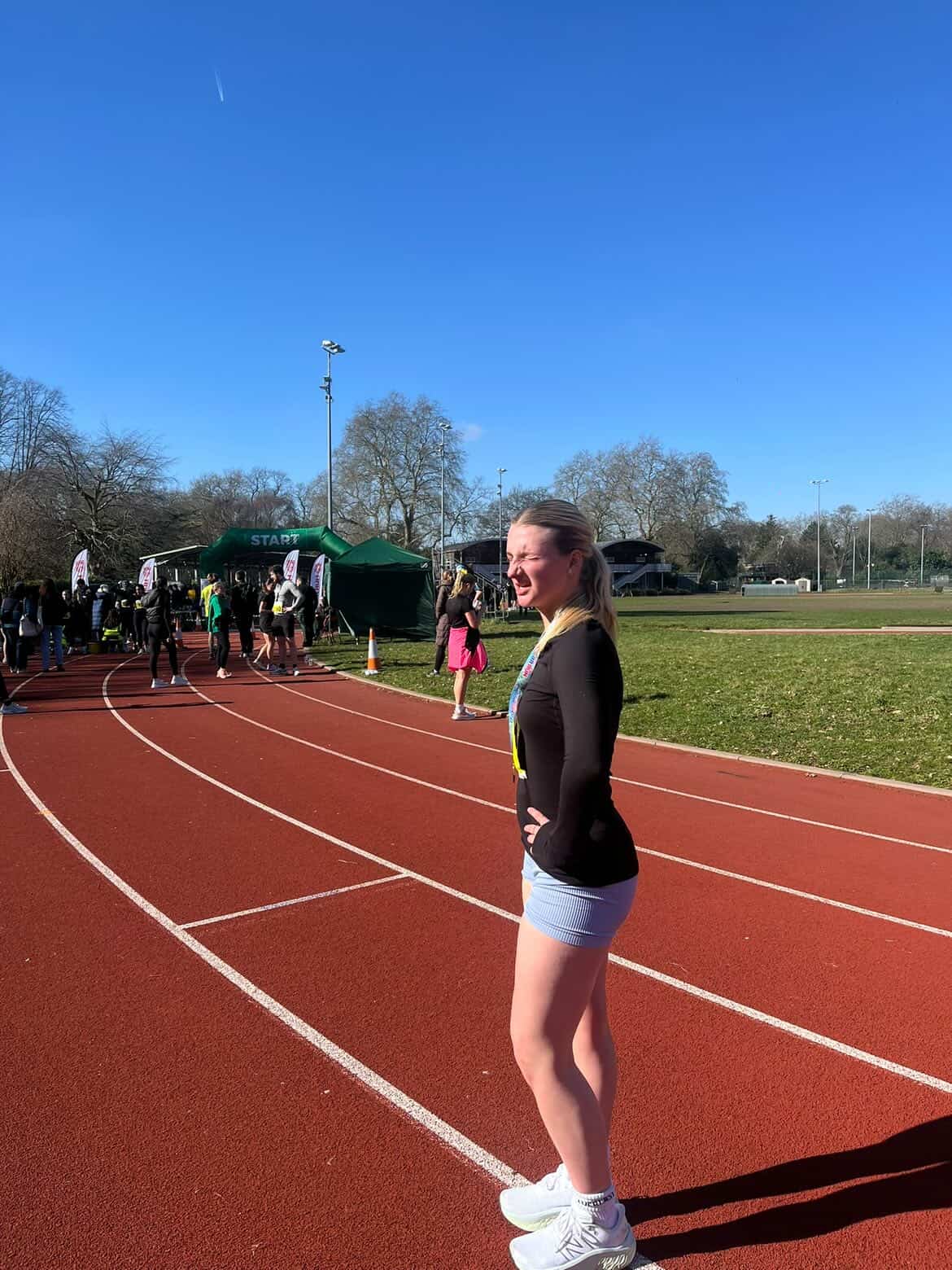 A photo of Isla standing on a running track in the sun.