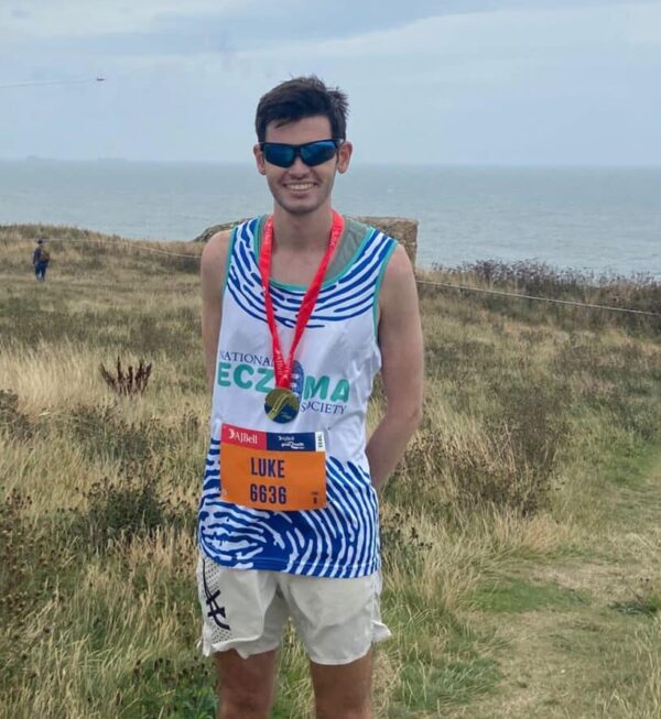 A man in a running vest standing in front of a beach.