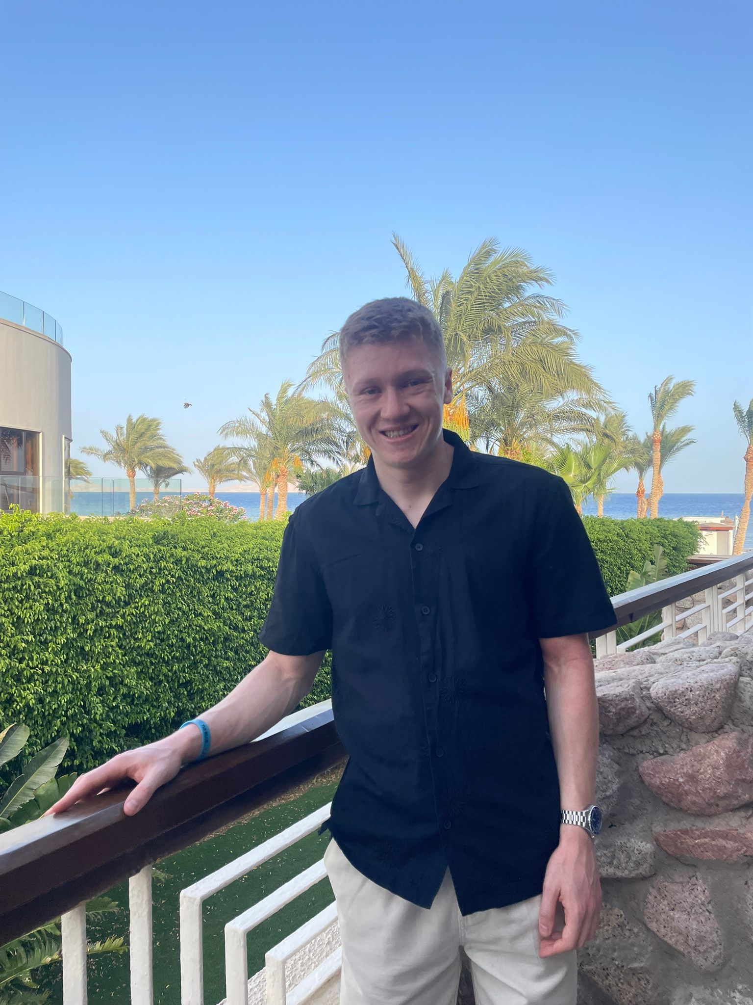 A picture of a man standinginfront of a tropical hotel.