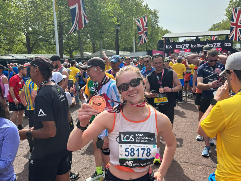 A runner in an eczema uk vest posing with her medal