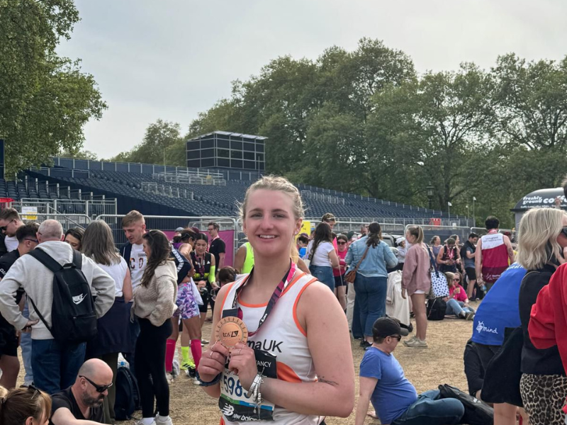 A runner in an eczema uk vest posing with her medal