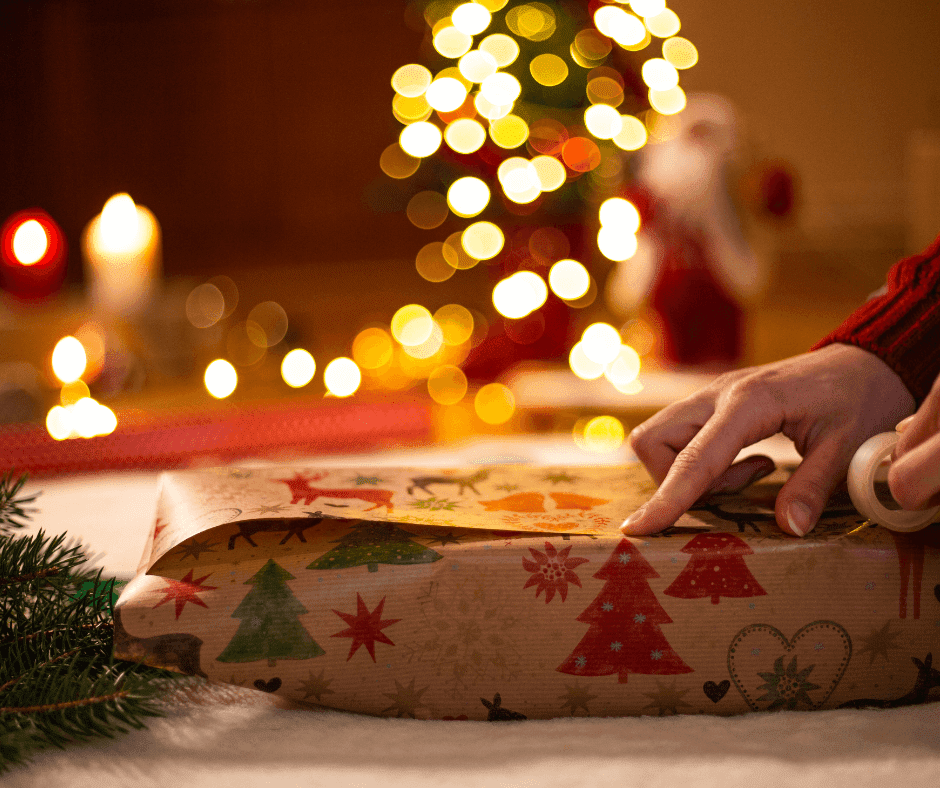 Someone wrapping a Christmas present next to a Christmas tree